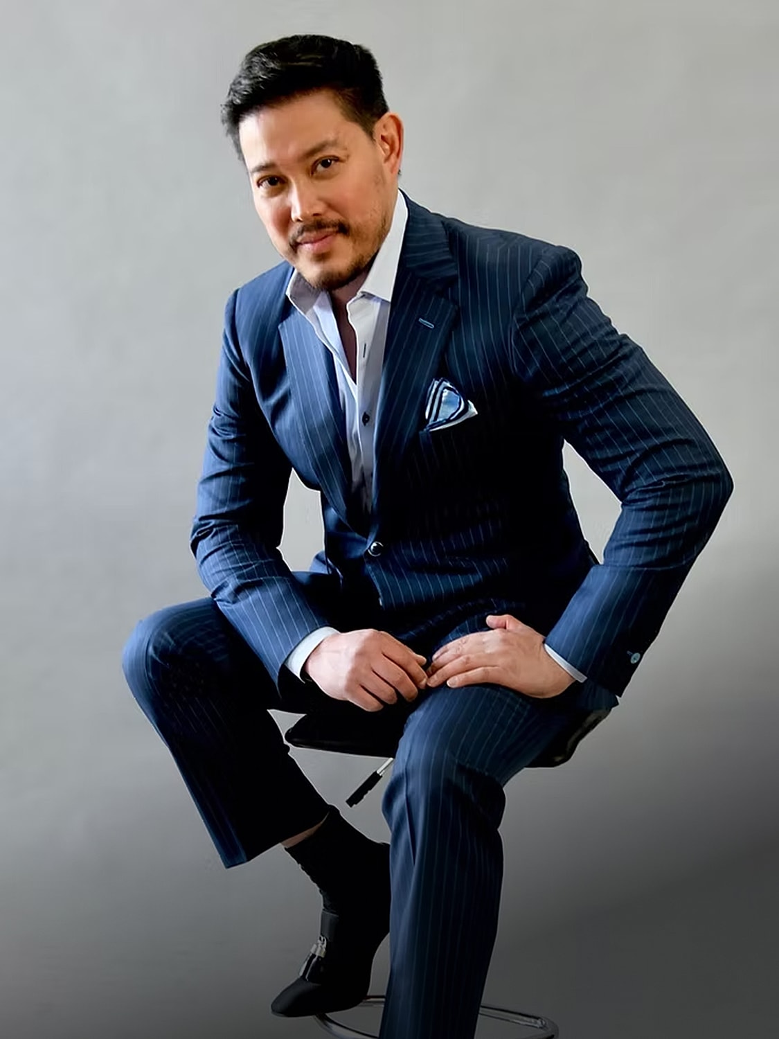 Man in a pinstripe suit sitting on a stool.
